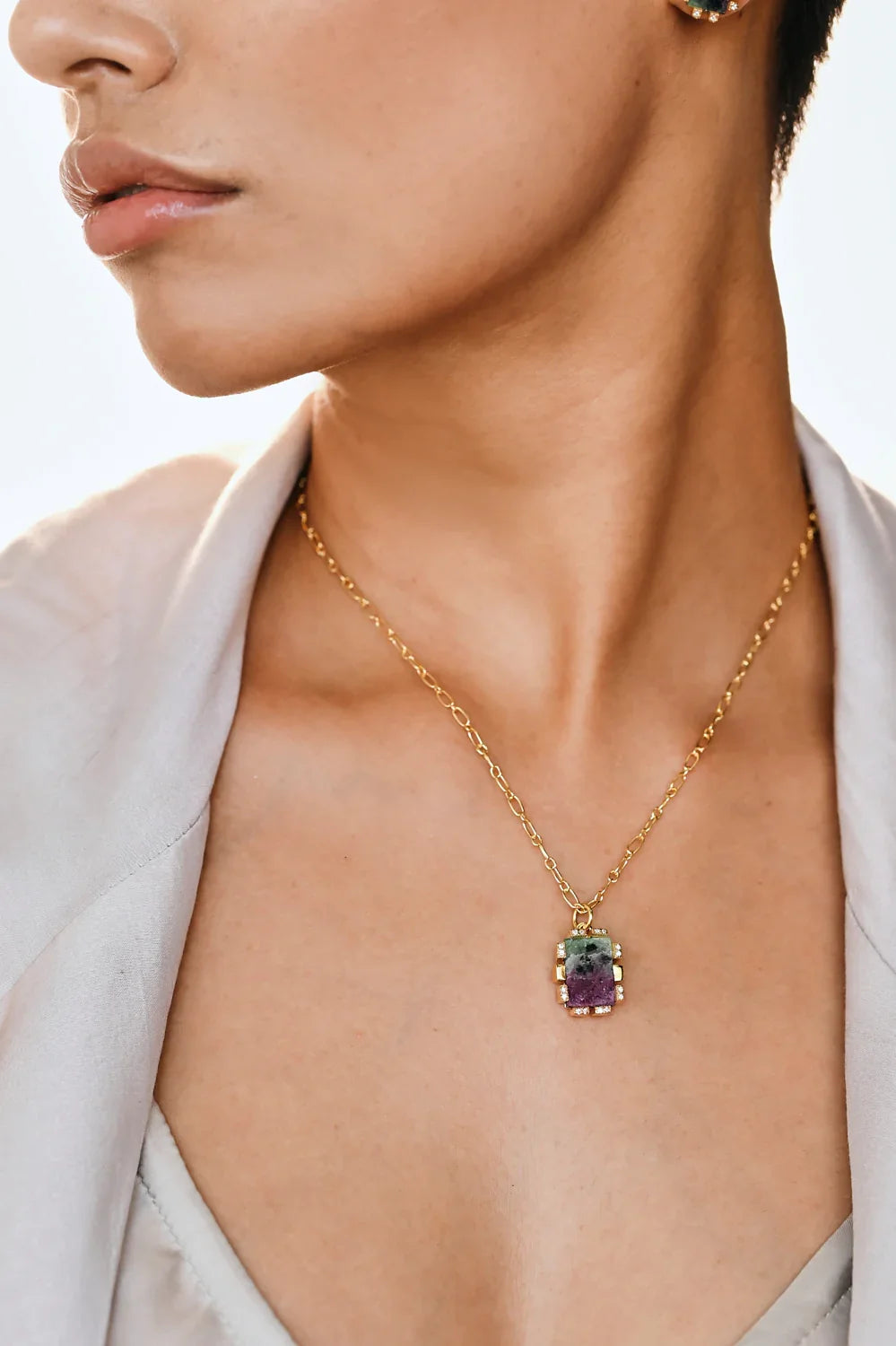 Gold chain necklace with a gemstone pendant worn open-necked