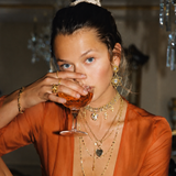 Woman in an orange outfit drinking from a cocktail glass in a dimly lit room.