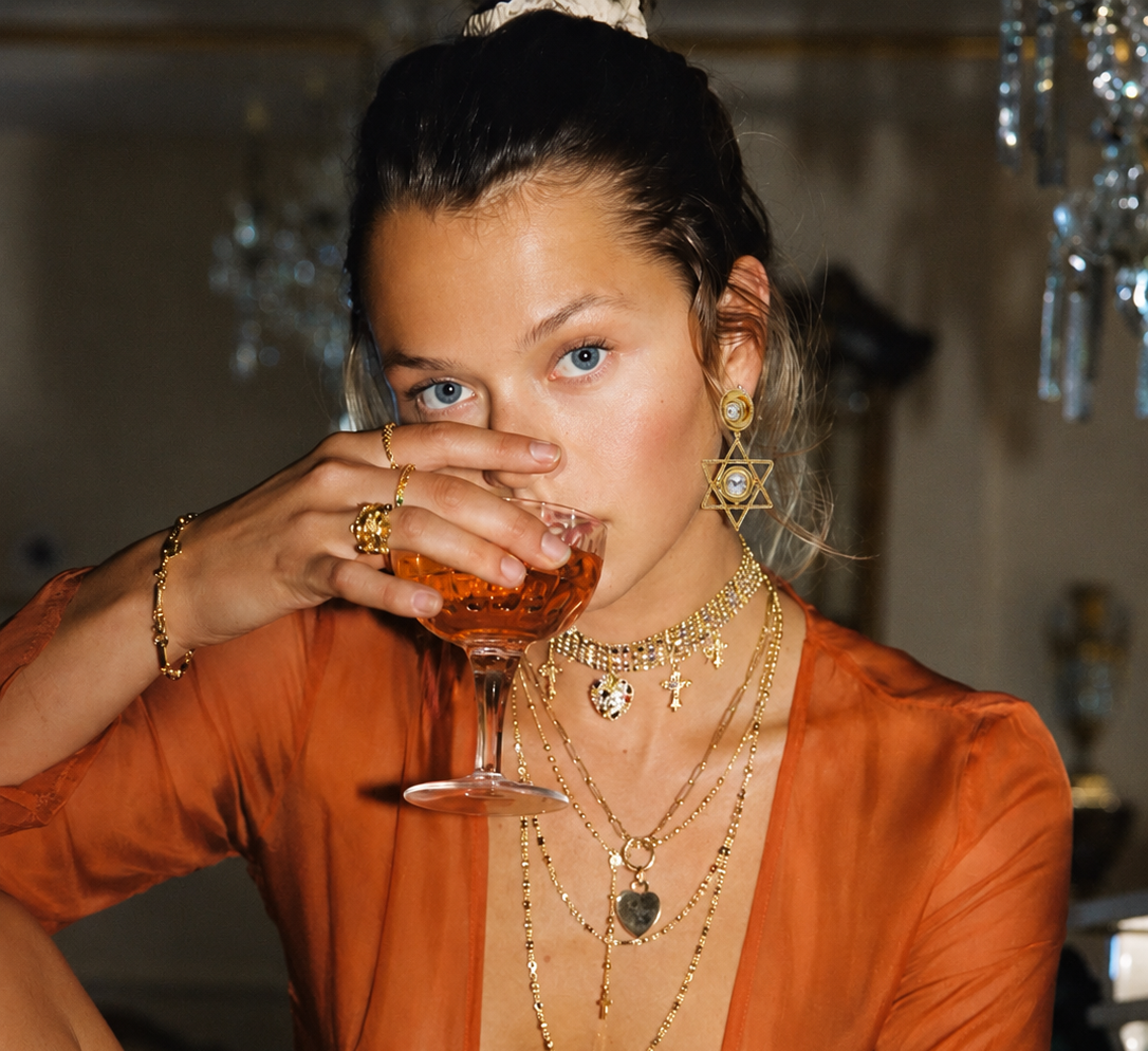 Woman in an orange outfit drinking from a cocktail glass in a dimly lit room.